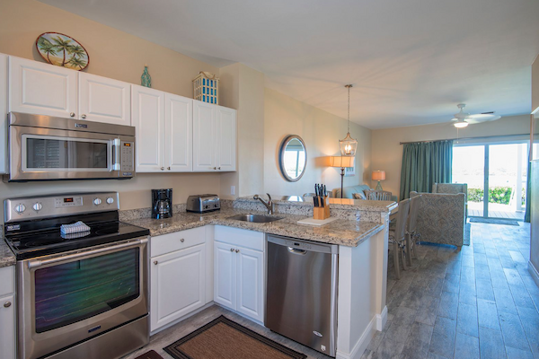 A modern kitchen and open dining area with white cabinets, stainless steel appliances, and light décor; view of living room and balcony.