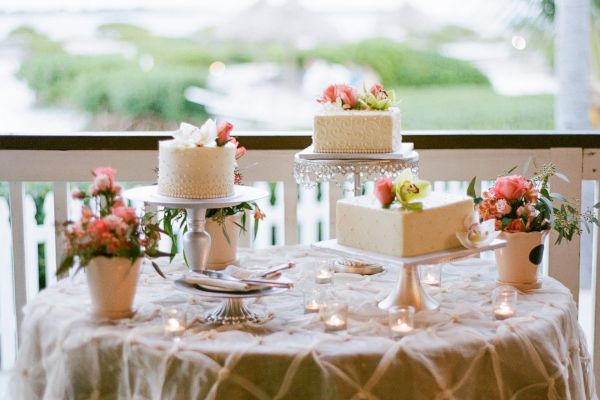 A beautifully decorated table with cakes and flowers, set outdoors with a scenic background of greenery and water, perfect for a celebration.