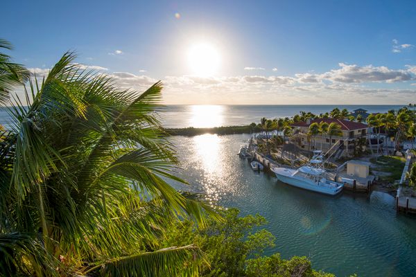 The image shows a serene waterfront view with palm trees, a docked boat, and houses by the water during sunset, creating a tranquil atmosphere.