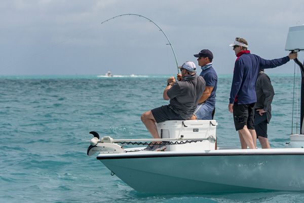 Several men are on a small boat in the ocean; one is holding a fishing rod, seemingly catching something, while others watch.