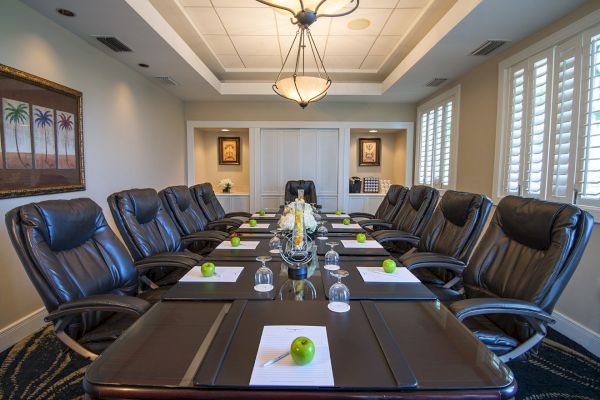 The image shows a modern conference room with a long table, leather chairs, notepads, water glasses, and green apples in front of each chair.