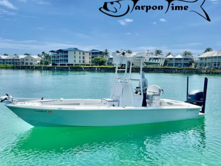 The image shows a white fishing boat on clear turquoise water, with buildings and palm trees in the background and a logo of a fish saying 