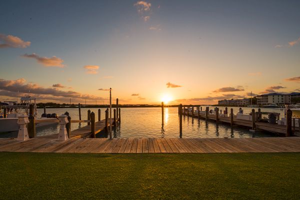 The image shows a sunset view from a dock with boats, calm water, and a partially cloudy sky, creating a serene and picturesque scene.