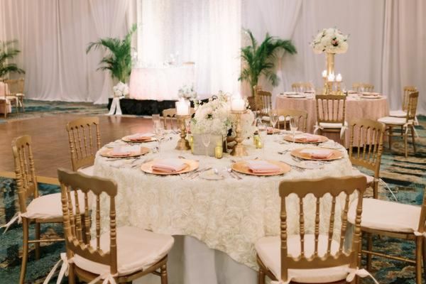 The image shows an elegantly decorated banquet hall with round tables set for an event, featuring floral arrangements and soft lighting.