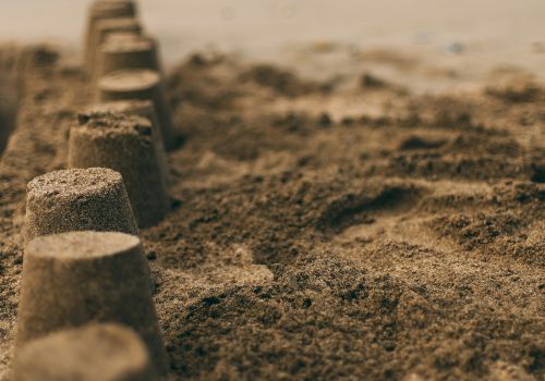 The image shows a row of sandcastles lined up on a beach with the ocean and waves in the background.