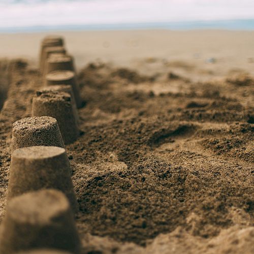 The image shows a row of sandcastles lined up on a beach with the ocean and waves in the background.