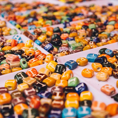 The image shows trays filled with colorful, lettered beads, possibly for crafting or jewelry-making purposes, arranged in a random order.