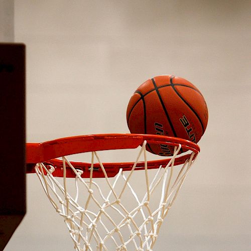 A basketball is seen resting on the rim of a basketball hoop with a net, indicating a close or potential successful shot.