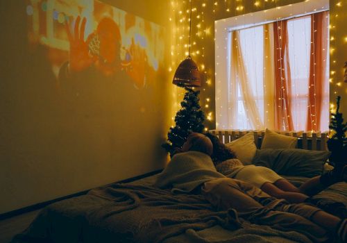 A cozy room with a bed, fairy lights, a projection on the wall, and a person sleeping.