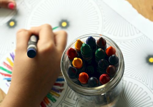 A child coloring with crayons from a jar on a patterned paper, with vibrant colors being used for the design.