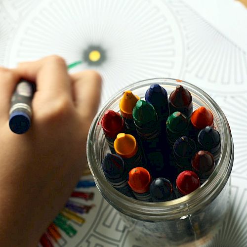 A child coloring with crayons from a jar on a patterned paper, with vibrant colors being used for the design.