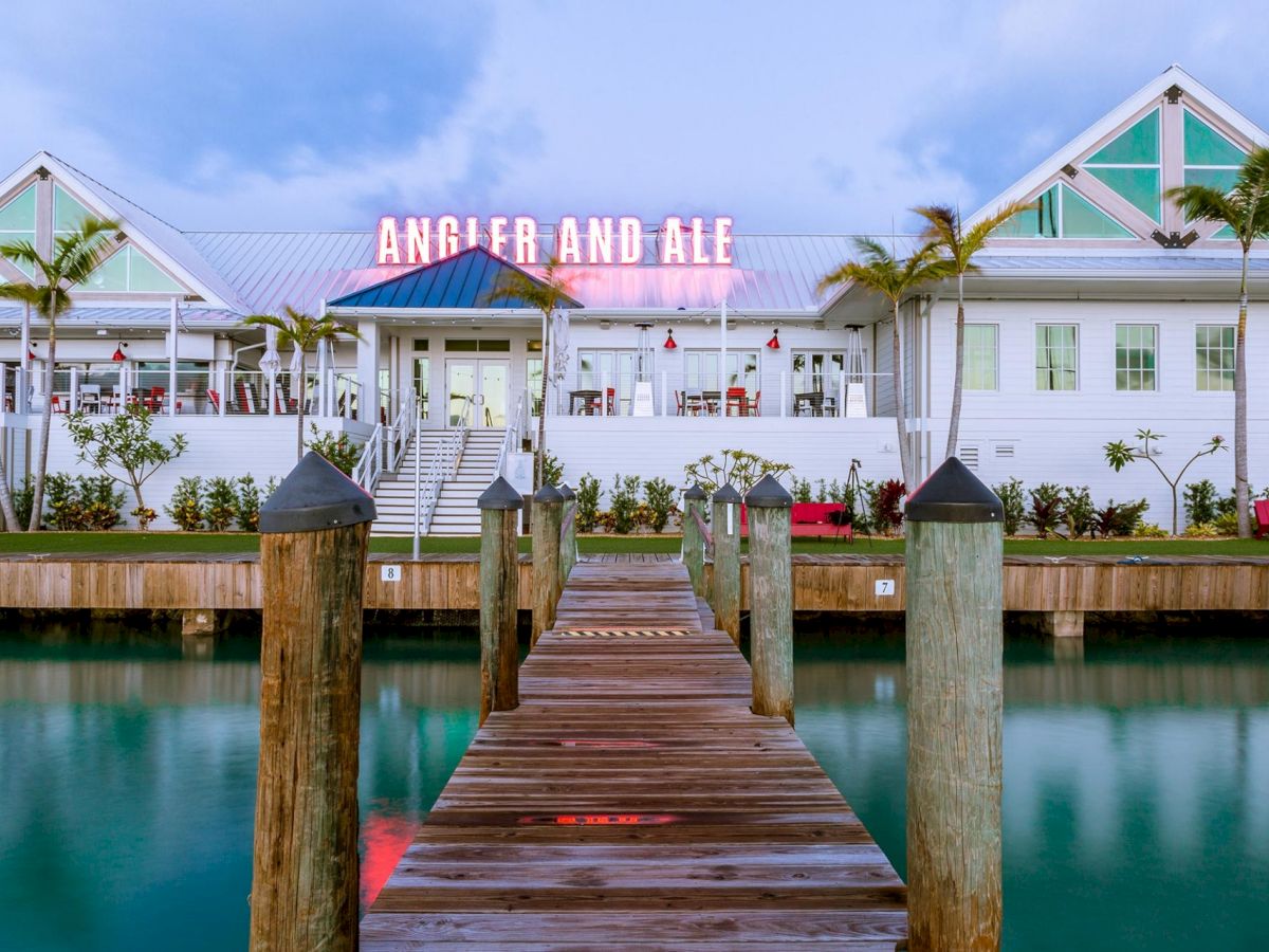 A wooden dock leads to a waterfront building with a neon sign that reads 