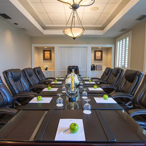 This image depicts a modern conference room with a long table, leather chairs, notepads with green apples, and a decorative chandelier.