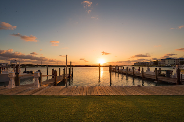 A serene marina scene at sunset, with wooden docks extending into calm water under a clear sky with scattered clouds in the background.